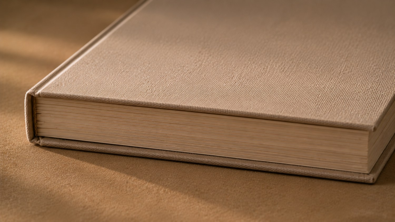 A linen-bound hardcover resting on a warm surface in low light, its gilded page edges and cloth spine catching the light.